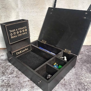 May include: A black wooden dice box with an open lid and multiple compartments. The box has a dice tower with the text "TAKE A CHANCE ROLL THE DICE" and the name "DeKanter". The box contains dice and game pieces.
