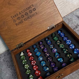May include: A wooden dice box with a hinged lid, filled with multi-sided dice in red, blue, green, and purple. The lid is engraved with the text "TAKE A CHANCE ROLL THE DICE". The dice are arranged in rows within a black foam insert.