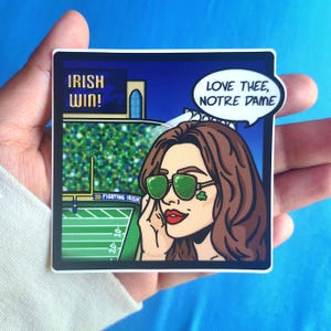 May include: A square sticker featuring a cartoon illustration of a woman wearing green sunglasses and a shamrock. The background depicts a football field and the text "IRISH WIN!" and "LOVE THEE, NOTRE DAME".