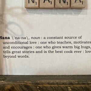 May include: A framed print with a definition of the word "Nana" in black text on a white background. The definition reads: "Nana /'na-na/, noun: a constant source of unconditional love: one who teaches, motivates, and encourages: one who gives warm big hugs, tells great stories and is the best cook ever: loved beyond words."