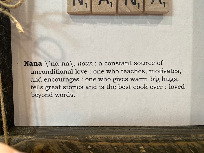 May include: A framed print with a definition of the word "Nana" in black text on a white background. The definition reads: "Nana /'na-na/, noun: a constant source of unconditional love: one who teaches, motivates, and encourages: one who gives warm big hugs, tells great stories and is the best cook ever: loved beyond words."