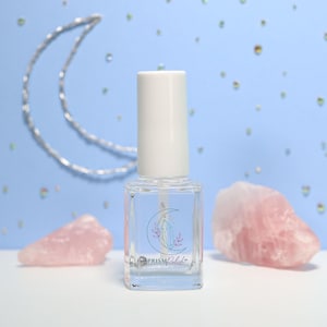 May include: A clear glass bottle of nail polish with a white cap. The bottle has a label with a crescent moon and a crystal design. The label also says "PRISM Polish".