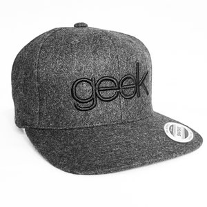Puede incluir: Una gorra de béisbol de visera plana gris y negra con la palabra "geek" bordada en negro en la parte delantera.