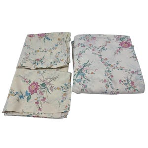 Może przedstawiać: Zestaw kremowych prześcieradeł z kwiatowym wzorem. Prześcieradła mają różowe, niebieskie i żółte kwiaty z zielonymi liśćmi. Kwiaty ułożone są w powtarzający się wzór na tkaninie.