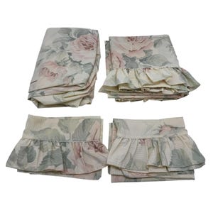 May include: A floral bed linen set with a rose design in pink, green, and cream. The set includes folded sheets and pillowcases with ruffled edges, giving a vintage look. The linens are made of a soft, textured fabric, suitable for a double or king-size bed.