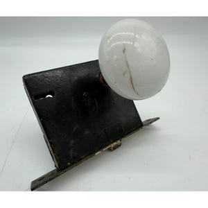 Könnte beinhalten: Antikes schwarzes Metalltürschloss mit einem weißen Porzellanknopf. Das Schloss hat ein Schlüsselloch und ein dekoratives Design.