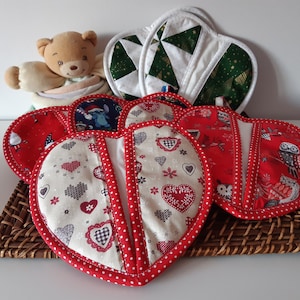 Peut inclure: Un ensemble de six maniques en forme de cœur avec différents motifs sur le thème des fêtes. Les maniques sont rouges et blanches avec un fond blanc et une bordure rouge. Les motifs comprennent des cœurs, des flocons de neige, des hiboux et un sapin de Noël.