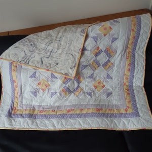 Peut inclure: Une courtepointe blanche avec un motif géométrique violet et jaune. La courtepointe a un dos gris clair et une bordure violette et jaune.