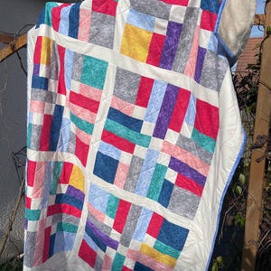 Peut inclure: Une courtepointe en patchwork avec un fond blanc et des carrés de différentes couleurs, notamment rouge, bleu, vert, jaune, violet et gris.