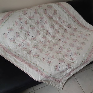 Peut inclure: Une courtepointe blanche avec un motif floral rose et vert. La courtepointe est faite de carrés et de triangles et a une texture matelassée.