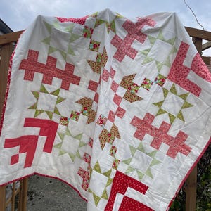 Peut inclure: Une courtepointe blanche avec un motif de patchwork en tissu floral rouge, rose et vert. La courtepointe est accrochée à une clôture en bois.
