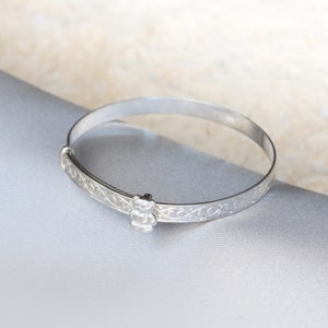 May include: A silver baby bangle with a bear charm. The bangle is engraved with a Celtic knot design.