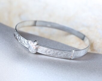 Pode incluir: Um bracelete de bebé de prata com um pequeno amuleto de urso gravado. O bracelete tem um design delicado e intrincado.