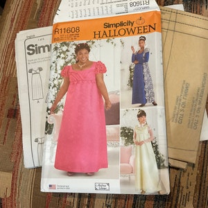 May include: A Simplicity Halloween sewing pattern with three different costume designs. The pattern is for sizes 22 to 28. The costumes include a pink gown, a blue gown with lace, and a white gown with a lace bodice.