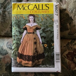 May include: A McCall's Costumes sewing pattern for a dress, featuring a woman wearing a brown dress with a black lace trim and a sunflower design. The pattern number is M8017 and the size is E5 (14-16-18-20-22).