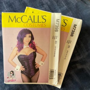 May include: A McCall's Costumes sewing pattern featuring a woman in a purple and black corset with white cuffs and collar. The pattern includes sizes A5 and E5. The cover is yellow and white.