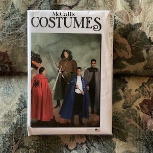 May include: McCall's Costumes sewing pattern for three capes. The pattern is for sizes S-M-L-XL-XXL. The pattern shows three people wearing the capes. One person is wearing a red cape with a dragon design, another is wearing a brown cape with a hood, and the third is wearing a blue cape with a white collar.