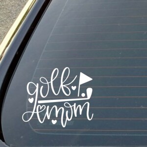 Pode incluir: Adesivo de vinil branco com o texto "golf mom" em fonte cursiva. Um taco de golfe e uma bandeira est&atilde;o inclu&iacute;dos no design, juntamente com v&aacute;rios cora&ccedil;&otilde;es pequenos.