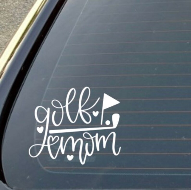 Pode incluir: Adesivo de vinil branco com o texto "golf mom" em fonte cursiva. Um taco de golfe e uma bandeira est&atilde;o inclu&iacute;dos no design, juntamente com v&aacute;rios cora&ccedil;&otilde;es pequenos.