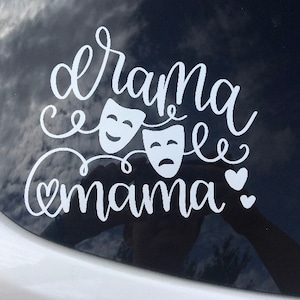 May include: White vinyl decal with the text "drama mama" and two theatrical masks, one smiling and one frowning. There are two small hearts to the right of the text.