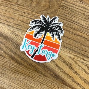 May include: A sticker with a palm tree silhouette and a sunset design. The text "Key Largo" is written in a cursive font.