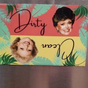 K&ouml;nnte beinhalten: Ein rosa und gelber K&uuml;hlschrankmagnet mit einem tropischen Blattdesign. Der Magnet zeigt zwei Bilder einer Frau mit blonden Haaren und den Text "Dirty Joan".