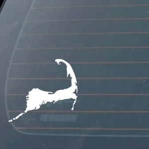 May include: White vinyl decal of the outline of Cape Cod, Massachusetts, on a dark gray car window.
