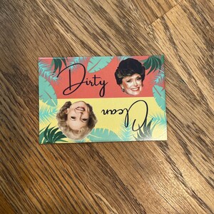 K&ouml;nnte beinhalten: Ein Magnet mit rosa und gelbem Hintergrund, der zwei Bilder einer Frau mit blonden Haaren zeigt. Der Text "Dirty" und "Dean" ist in schwarzer Kursivschrift auf dem Magneten geschrieben.