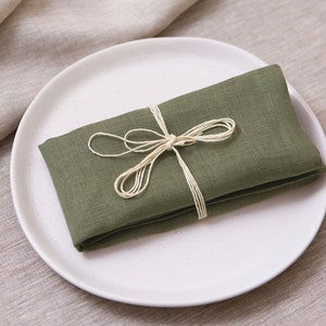 May include: A folded green linen napkin tied with twine, resting on a white plate.