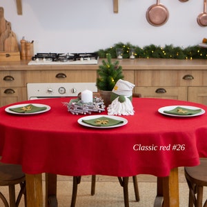 May include: A round red tablecloth covers a wooden table set for a festive occasion. White plates with green napkins and decorative accents are arranged around a small Christmas tree and a gnome. The text "Classic red #26" is visible.