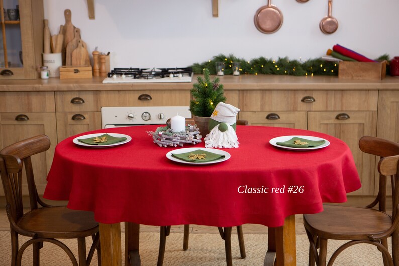 May include: A round red tablecloth covers a wooden table set for a festive occasion. White plates with green napkins and decorative accents are arranged around a small Christmas tree and a gnome. The text "Classic red #26" is visible.