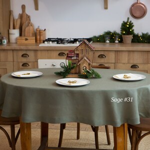 May include: A sage green round tablecloth on a wooden table, set with three white plates. A decorative wooden house and greenery are in the center. The text "Sage #31" is visible on the right side.
