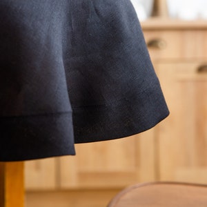 May include: Close-up of a dark navy blue linen tablecloth. The fabric drapes over a table, showcasing the texture and subtle sheen of the material. The hem is neatly stitched, adding a touch of elegance.