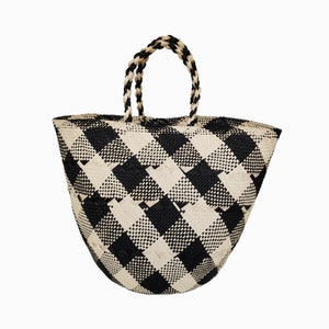 Puede incluir: Un bolso tote grande de cuadros negros y blancos con asas tejidas. El bolso est&aacute; hecho de un material natural y tiene un fondo redondeado.