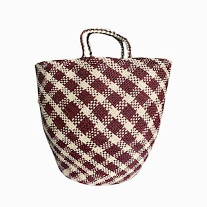 Puede incluir: Un bolso tote grande tejido con un patr&oacute;n de cuadros burdeos y blanco. El bolso tiene dos asas y est&aacute; hecho de fibras naturales.