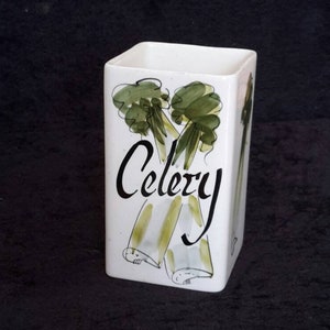 Może przedstawiać: Biały ceramiczny pojemnik kuchenny z ręcznie malowanym wzorem selera. Słowo "Celery" jest napisane czarnym pismem. Pojemnik jest prostokątny i wydaje się być akcesorium kuchennym w stylu vintage lub retro.
