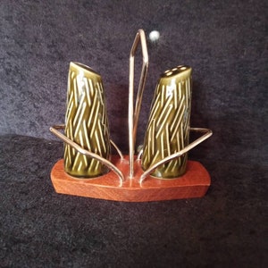 May include: A vintage salt and pepper shaker set. The olive green ceramic shakers have a textured, geometric design and sit on a wooden base. A gold-coloured metal handle and holder complete the set. The base measures approximately 13 cm long.