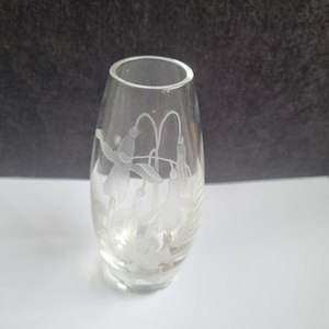 May include: Clear glass vase with an etched floral design. The vase has a rounded base and a slightly flared top. The etched design features stylized flowers and leaves, creating a delicate aesthetic. The vase is empty and sits on a white surface.