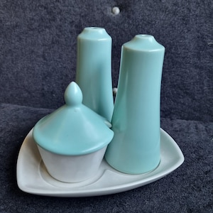 Puede incluir: Un juego de salero y pimentero de cerámica vintage con azucarero. El juego es de color azul claro con base blanca y bandeja blanca. Los saleros y pimenteros son altos y cilíndricos, mientras que el azucarero tiene tapa.