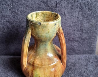 Pode incluir: Pequeno vaso de cerâmica artesanal, com corpo arredondado e duas alças arqueadas. Mistura de tons terrosos: castanho, amarelo e verde. Acabamento texturizado e craquelado na borda. Design rústico e artístico.