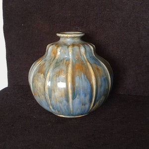 May include: A ceramic vase with a rounded form and a narrow neck. The vase has a blue and brown glaze with vertical ridges. The vase is a decorative item.
