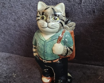 Peut inclure: Figurine en céramique représentant un chat habillé en golfeur, portant un sac de golf. Le chat porte une chemise verte, un pantalon noir et des chaussures marron. Le visage du chat a des yeux jaunes et des rayures noires.