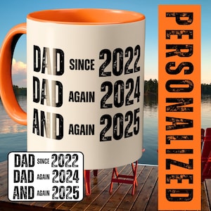 Op de afbeelding: Een witte keramische mok met een oranje binnenkant en oor. De mok heeft de tekst "DAD SINCE 2022, DAD AGAIN 2024, AND AGAIN 2025" in het zwart. Een kleinere versie van de tekst staat op een witte rechthoek. Het woord "PERSONALIZED" is verticaal op een oranje achtergrond gedrukt.