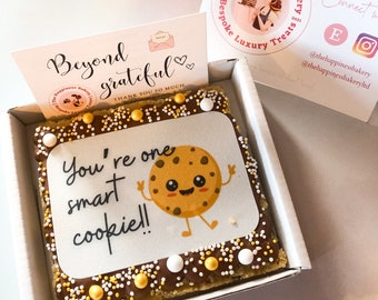 May include: A square cookie decorated with chocolate and sprinkles. The cookie has a printed image of a smiling cookie with the text "You're one smart cookie!"