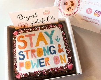 May include: A square brownie topped with pink and white sprinkles and a white icing sheet with the text "STAY STRONG & POWER ON" in colorful letters. The brownie is in a white box with a pink and white card that says "Beyond grateful".