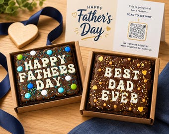 May include: Two square chocolate brownies in cardboard boxes, decorated with white frosting that spells out "HAPPY FATHERS DAY" and "BEST DAD EVER". A Father's Day card and a wooden heart are also in the image.