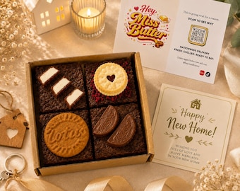 May include: A square cardboard box containing four dark chocolate brownies topped with various cookies and chocolate pieces. One brownie features white chocolate rectangles, another a heart-centered biscuit, a third a round Lotus cookie, and the last two chocolate wedges. Includes two printed cards.