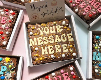 May include: Assortment of chocolate brownies with various toppings and messages. The brownies are in individual boxes and feature messages like "Thank You", "Your Message Here", and "Have a Great Day".