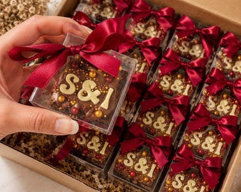 May include: A box of chocolate treats, each in a clear case and tied with a burgundy ribbon. The chocolate squares are decorated with white letters spelling "S&I" and colorful sprinkles. The box is brown.