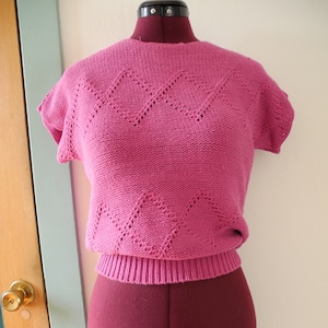 Peut inclure: Un pull rose en tricot à manches courtes et à motif en losange. Le pull est sur un mannequin.